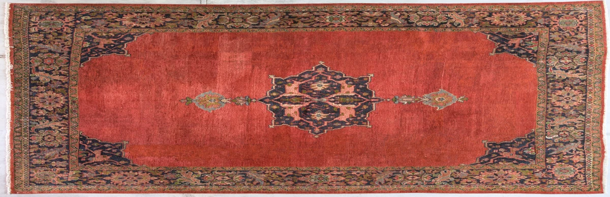 A wide antique carpet with a deep red field and a dark central medallion, photographed on the gallery floor